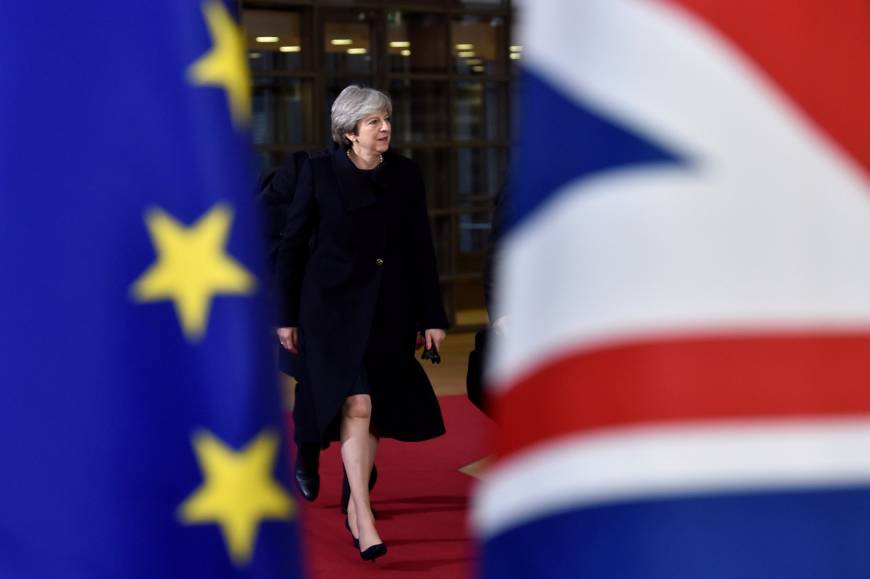 Theresa May, na reunião do Conselho Europeu, entre as bandeiras da União Europeia e a de seu país