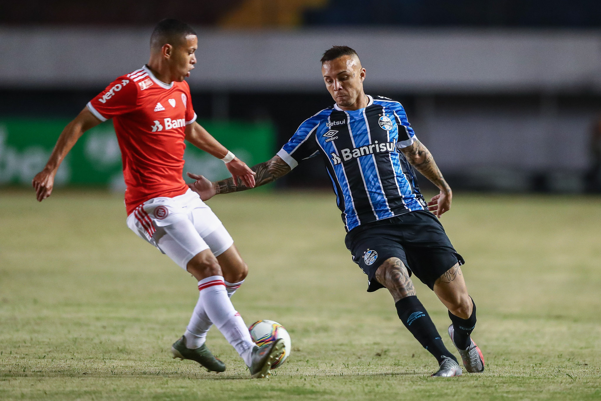 Um jogador do Internacional conduz a bola enquanto jogador do Grêmio se aproxima