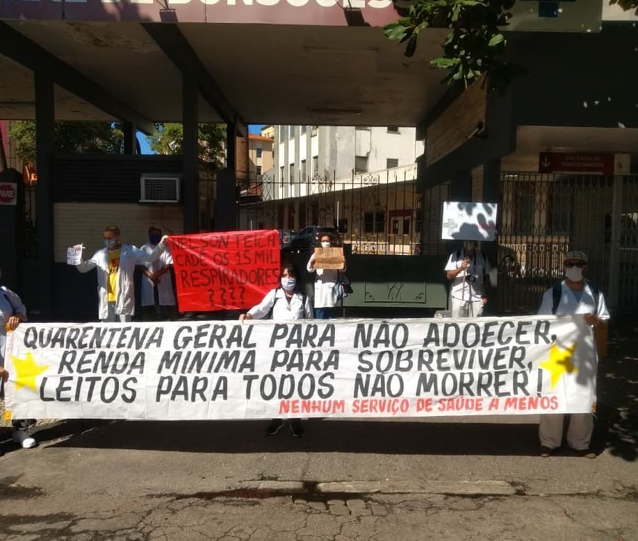 Trabalhadoras da saúde protestam em frente a um hospital no Rio de Janeiro. Na faixa que seguram, está escrito: "Quarentena geral para não adoecer. renda mínima para sobreviver, leitos para todos não morrer. Nenhum serviço de saúde a menos.