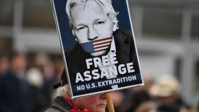 Homem segura um cartaz onde está a foto de Assange e o texto: Free Assange. No US Deportation