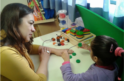 Professora acompanha aluna que utiliza brinquedos educativos, para estímulo da coordenação motora