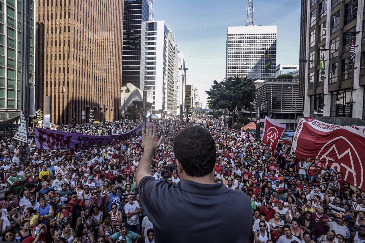 Guilherme Boulos, de costas para a foto, discursa para umma multidão na Avenida Paulista