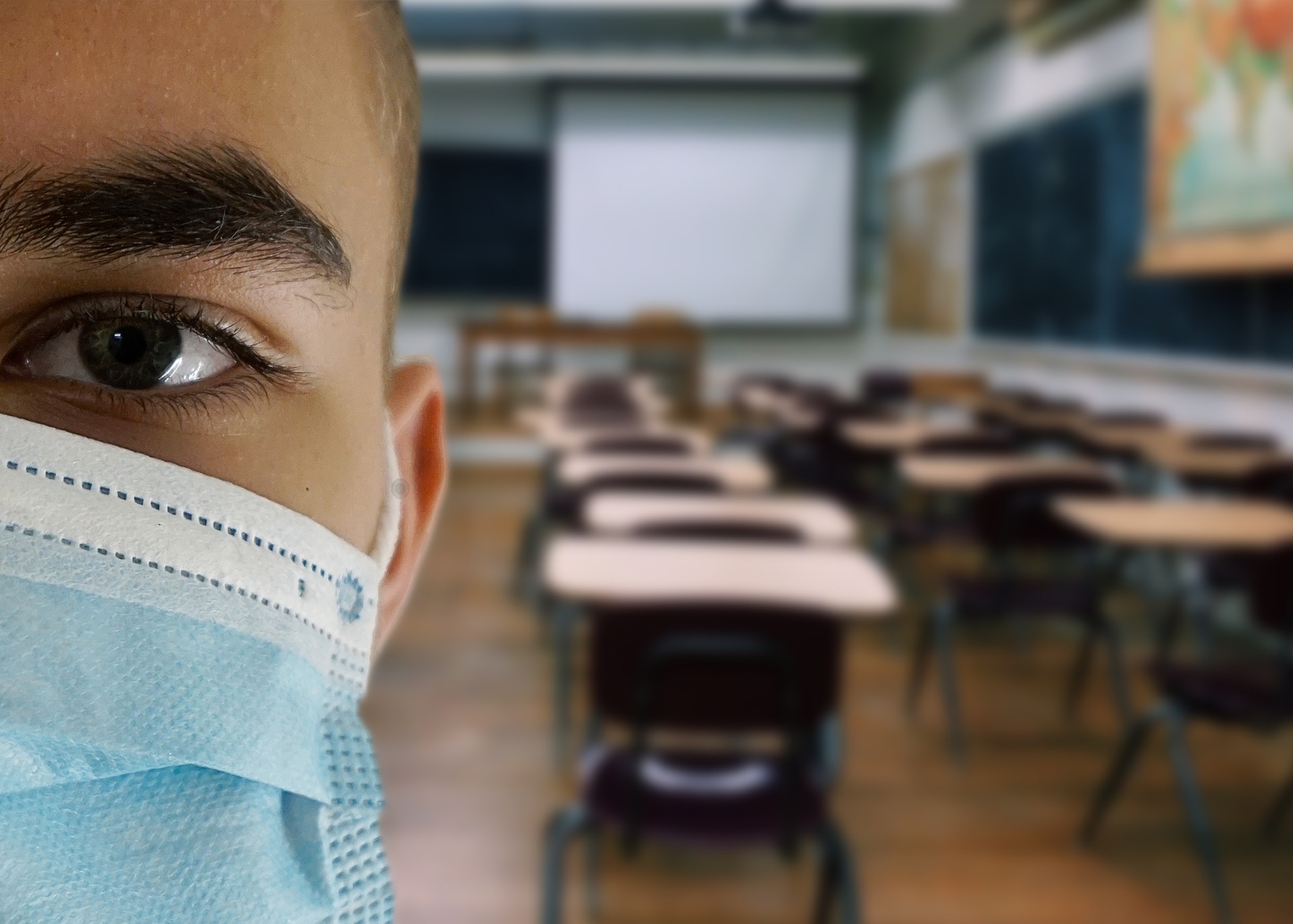 Detalhe do rosto de um aluno de máscara, ao fundo, uma sala de aula vazia