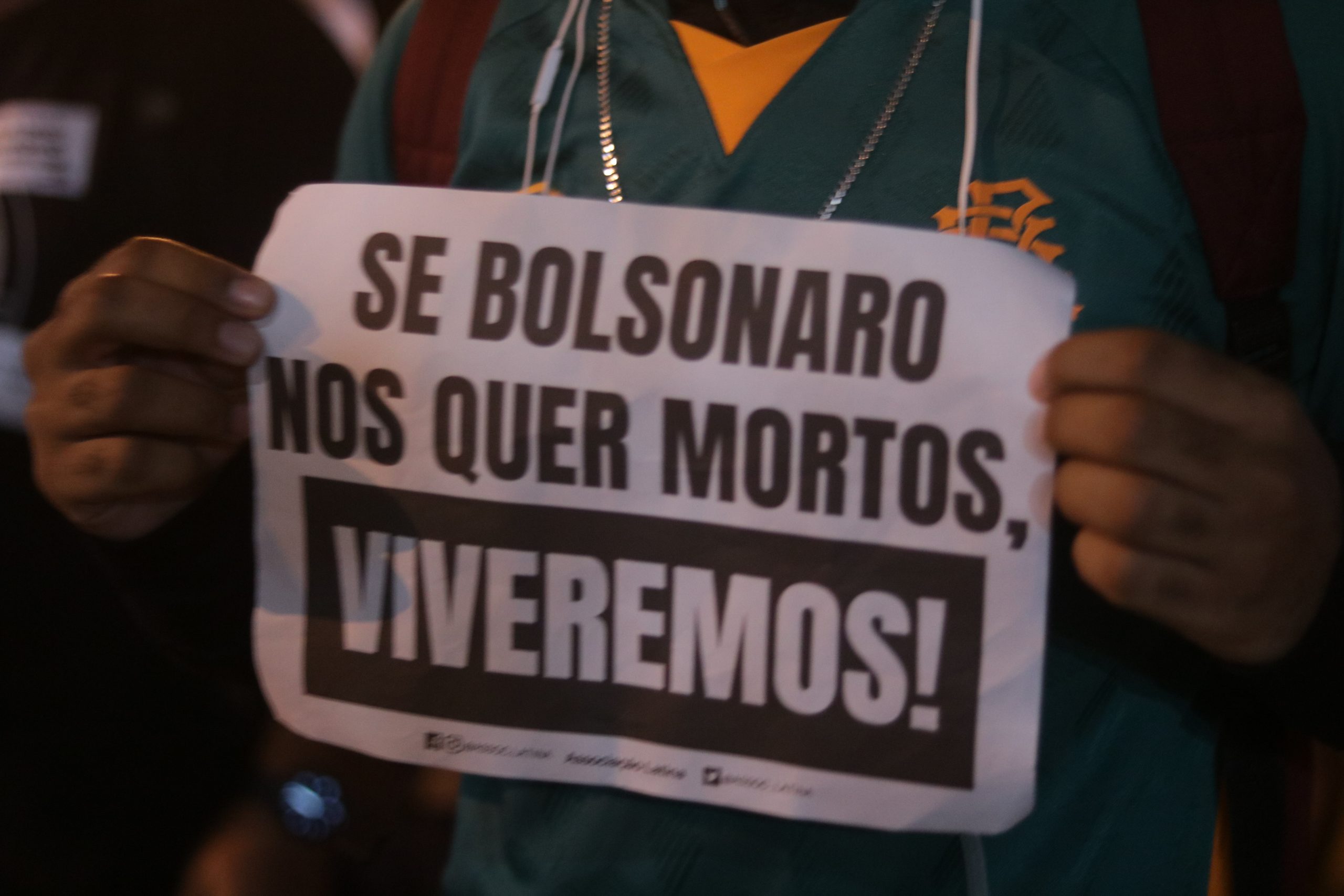 pessoa segura um cartaz, onde se lê: "Se Bolsonaro nos quer mortos, VIVEREMOS!"