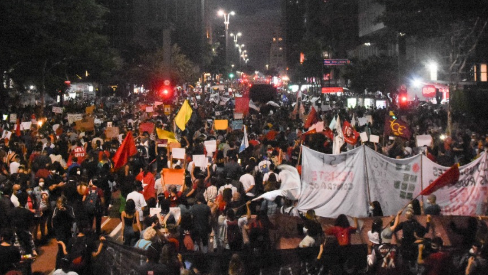 Foto mostra a Av. Paulista, à noite, tomada por manifestantes, de costas, caminhando.