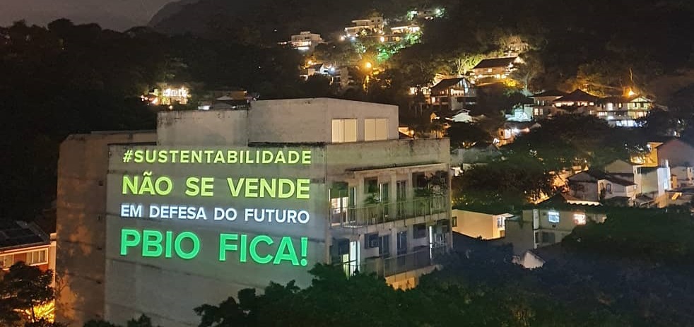 Em um prédio, estão projetados as frases: Sustentabilidade não se vende. Em defesa do futuro PNBIO FICA!