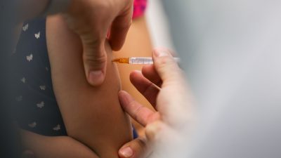 Imagem mostra um detalhe de uma injeção em um braço de uma criança.