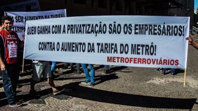 Trabalhadores em um ato com uma faixa branca, onde se lê: Quem ganha com a privatização são os empresários! contra o aumento da tarifa do metrô! Metroferroviários