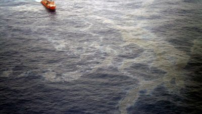 foto mostra um navio em direção a uma grande mancha de óleo no mar