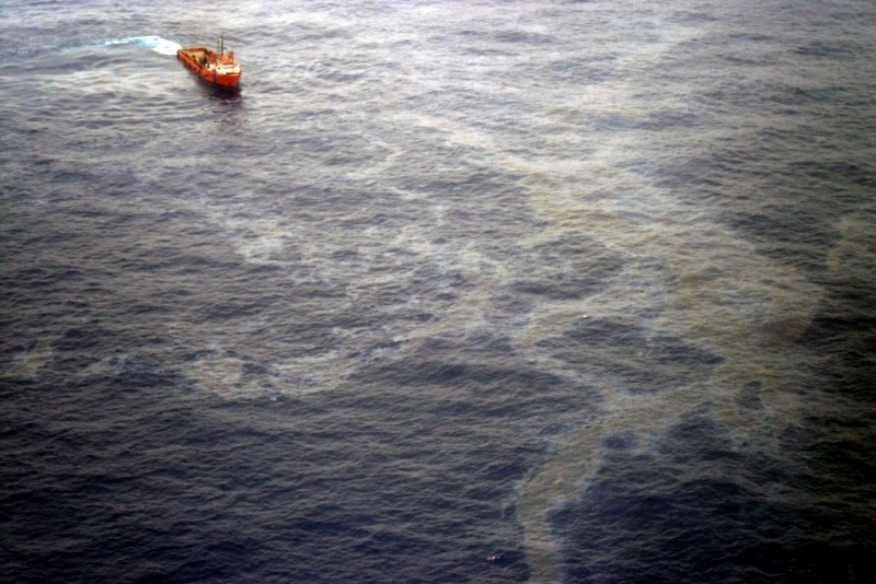 foto mostra um navio em direção a uma grande mancha de óleo no mar