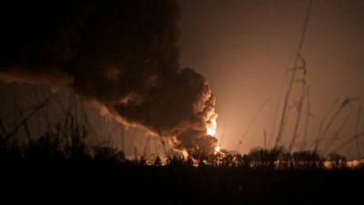 Foto noturna, mostra uma nuvem de fumaça ao longe iluminada por uma explosão do lado direito.