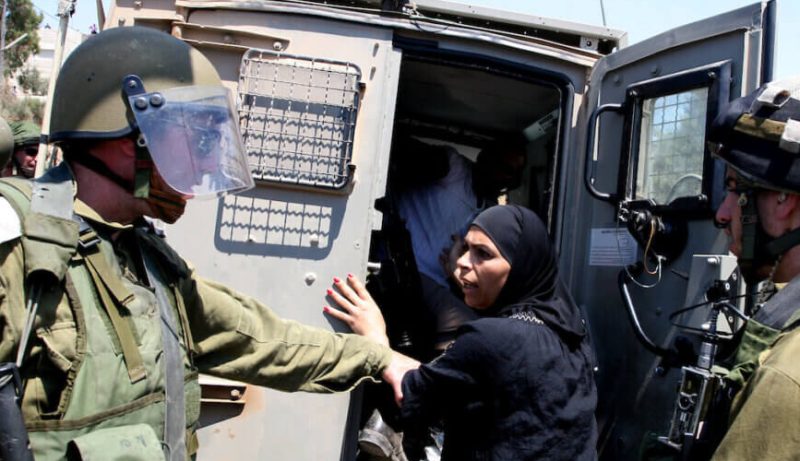 Palestina é presa por soldados, que a colocam em um veículo militar.