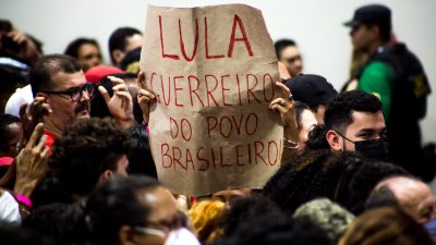 pessoa segura cartaz em comício com a frase: "Lula guerreiro do povo Brasileiro"