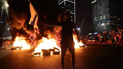 Um manifestante fica em frente a pneus em chamas na rodovia Ayalon, Tel Aviv. Dezenhas de milhares de manifestantes foram às ruas após o primeiro ministro Benjamin Netanyahu demitir o ministro da Defesa, Yoav Gallant, depois que ele pediu uma pausa na reforma judicial pelo governo